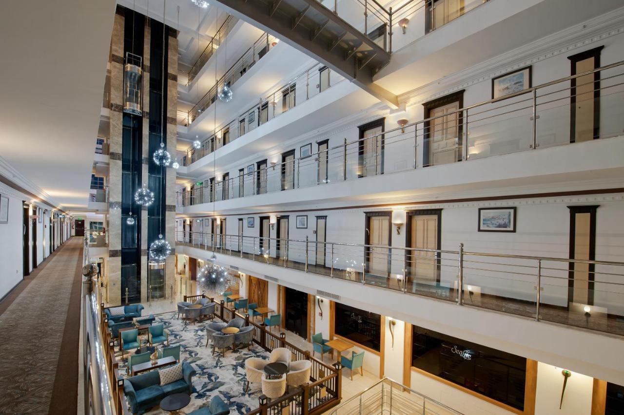 אנטליה Sealife Family Resort Hotel מראה חיצוני תמונה The photo shows the interior of a modern hotel or building featuring a multi-level atrium. There are several floors overlooking the central area, with glass railings providing a view of the spaces below. The decor includes stylish seating areas with 