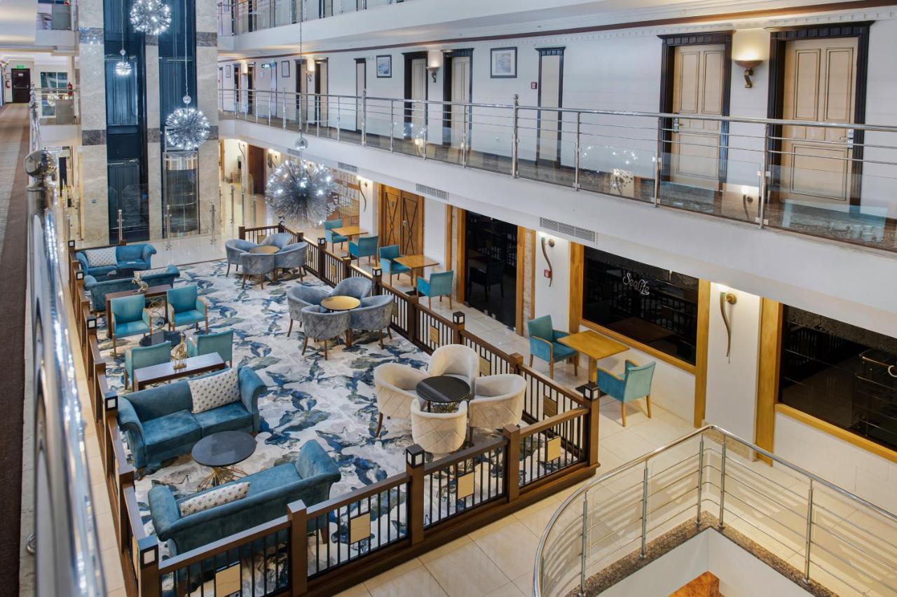 אנטליה Sealife Family Resort Hotel מראה חיצוני תמונה The photo shows the interior of a modern hotel lobby or lounge area. There are multiple seating arrangements with stylish teal chairs and cream-colored sofas set around tables. The floor features a large, decorative rug, and the walls have elegant fi