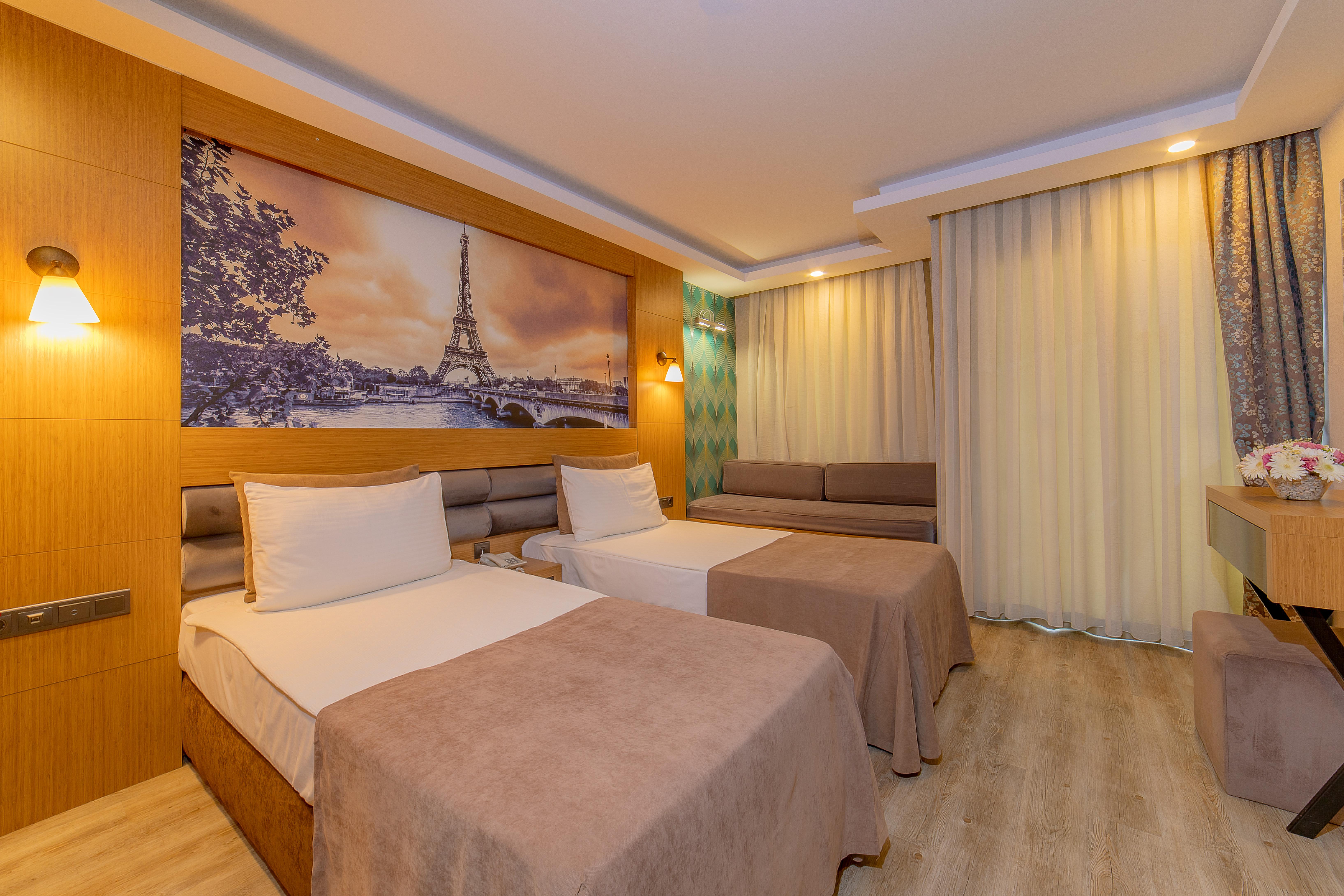 אנטליה Sealife Family Resort Hotel מראה חיצוני תמונה The photo shows a modern hotel room featuring two beds with beige bedspreads. There is a large wall mural depicting a scenic view of the Eiffel Tower in Paris. The room is well-lit, with soft lighting fixtures on the walls. To the right, there is a s