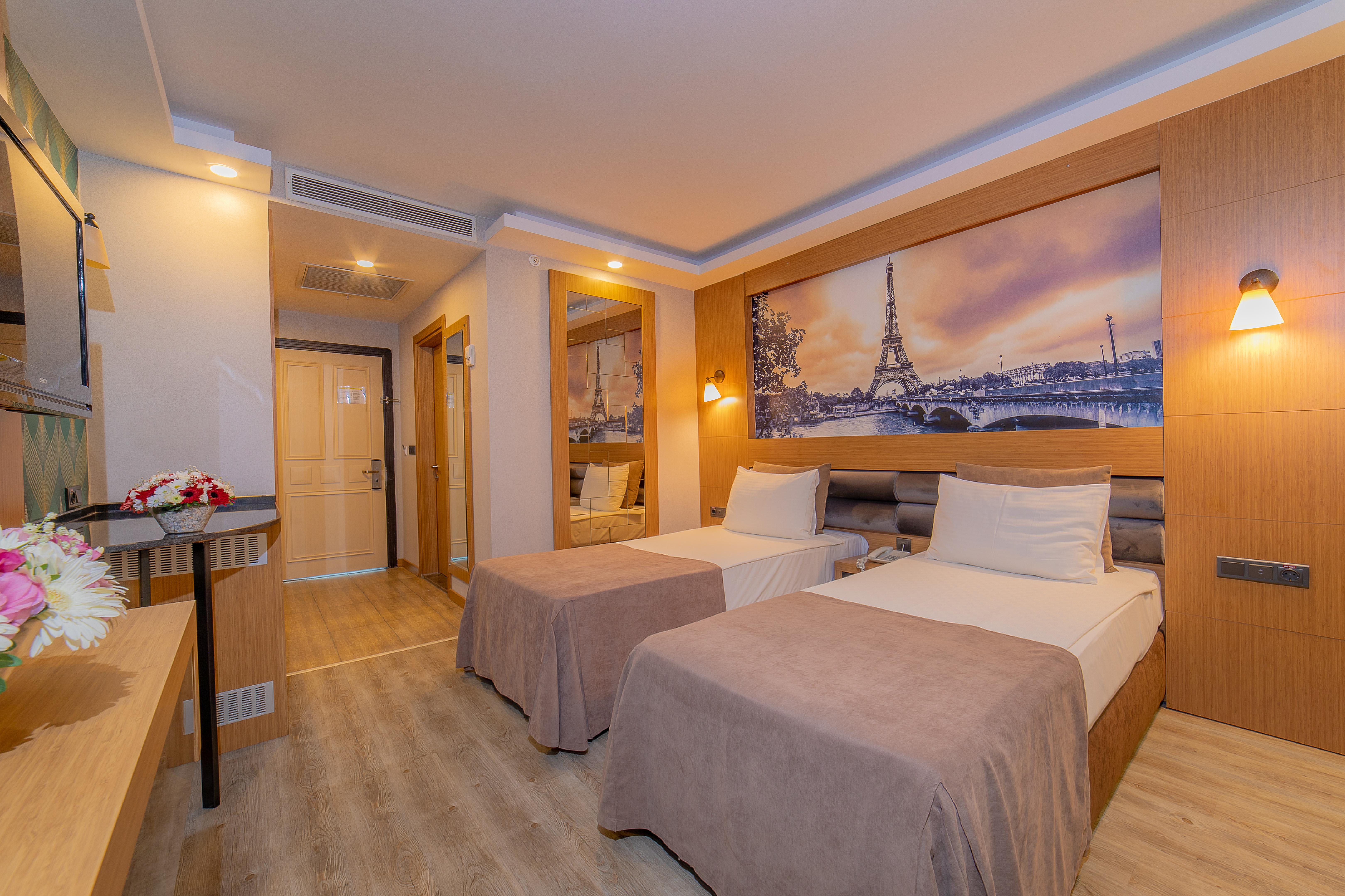 אנטליה Sealife Family Resort Hotel מראה חיצוני תמונה The photo depicts a modern hotel room featuring two single beds with light-colored bedspreads. The room has a warm and inviting ambiance, enhanced by the soft lighting. A large mirror is mounted on one wall, reflecting part of the room. Above the bed