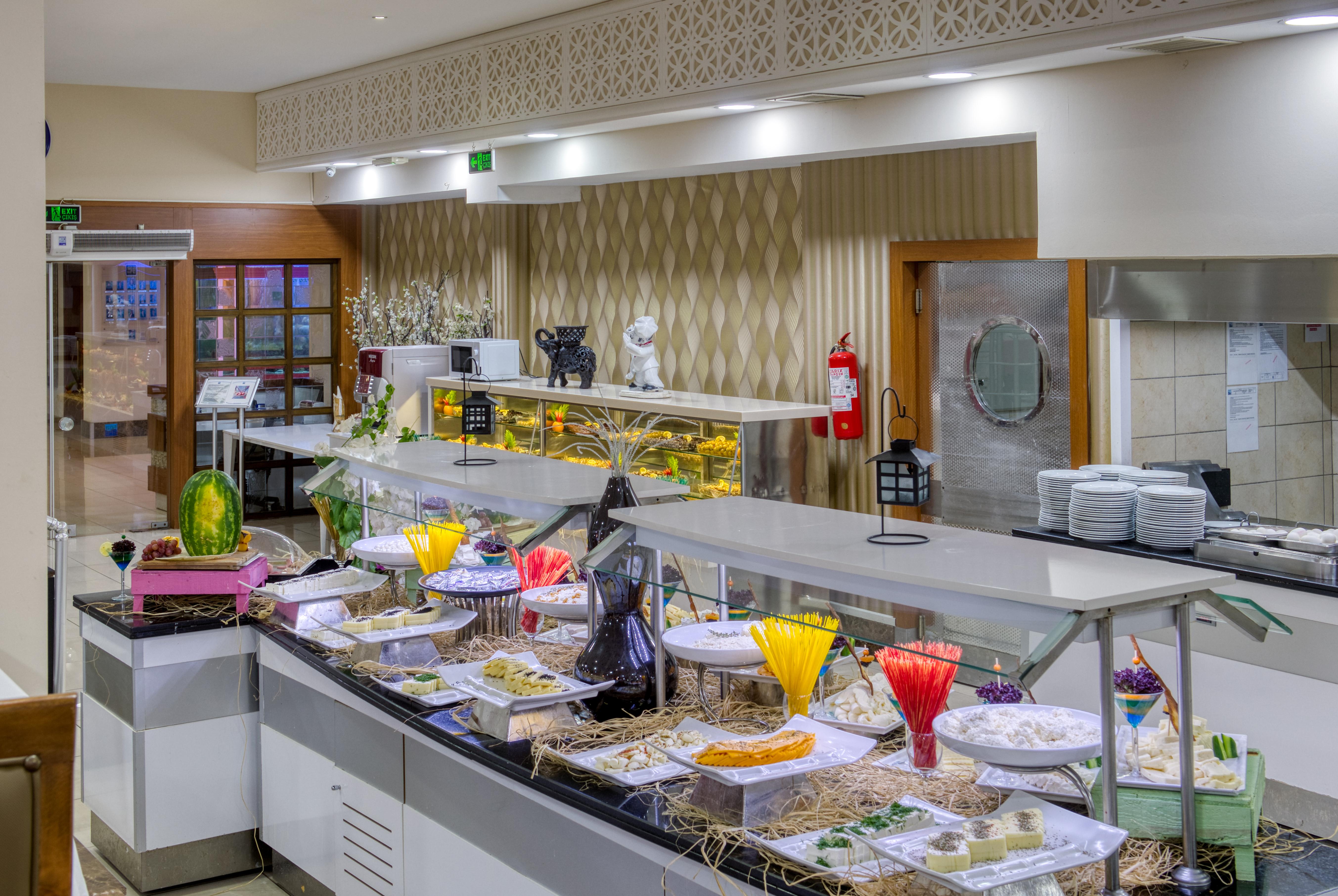 אנטליה Sealife Family Resort Hotel מראה חיצוני תמונה The image shows a buffet or dining area featuring a variety of colorful dishes and desserts displayed on a long serving counter. It includes decorative plates and containers filled with food items, likely intended for a buffet setup. The overall envi