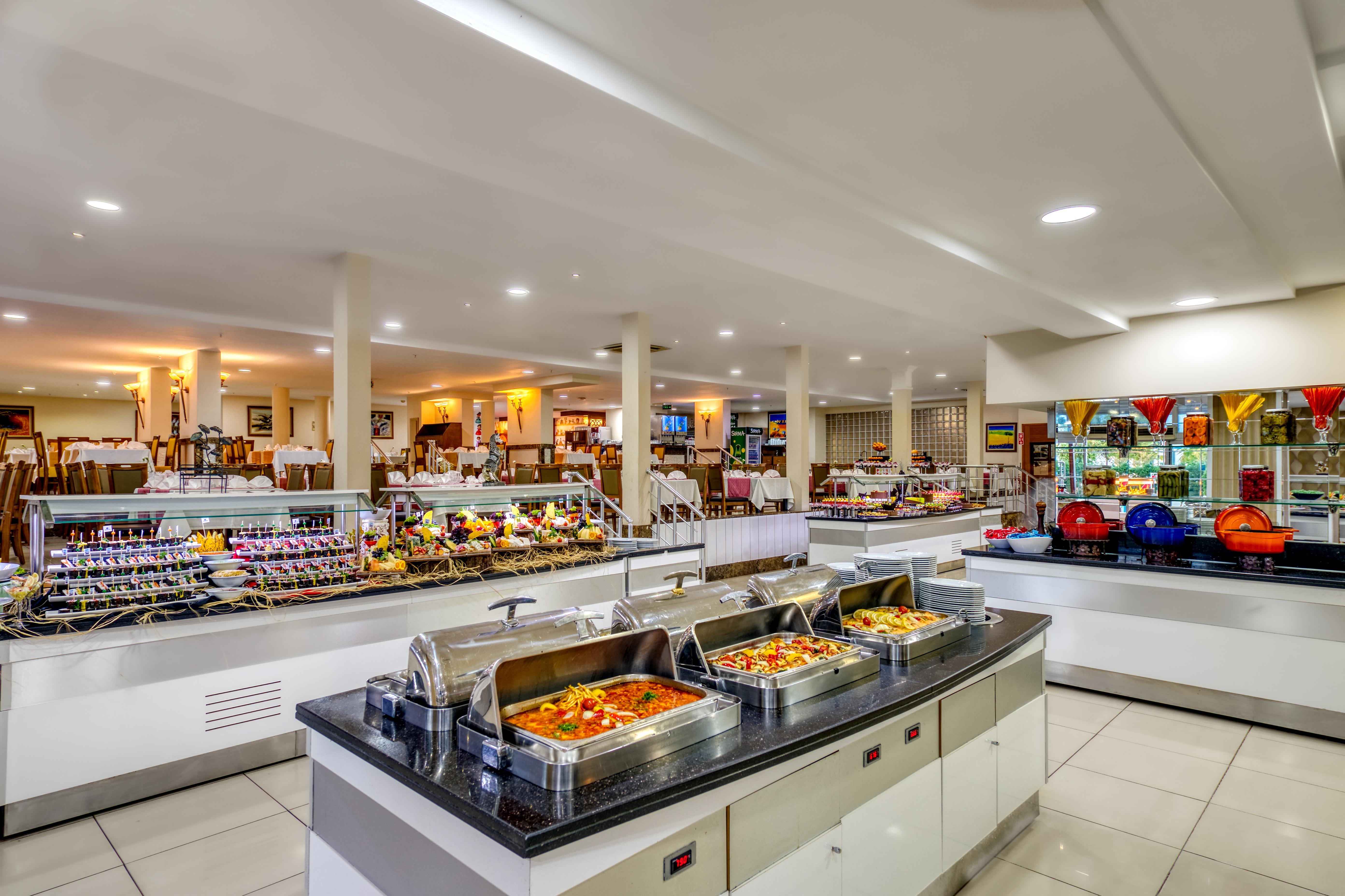 אנטליה Sealife Family Resort Hotel מראה חיצוני תמונה The photo shows a spacious buffet area in a restaurant. There are several food stations featuring a variety of dishes. In the foreground, there are chafing dishes that contain warm food, likely offering options like pasta, vegetables, or meats. Behin