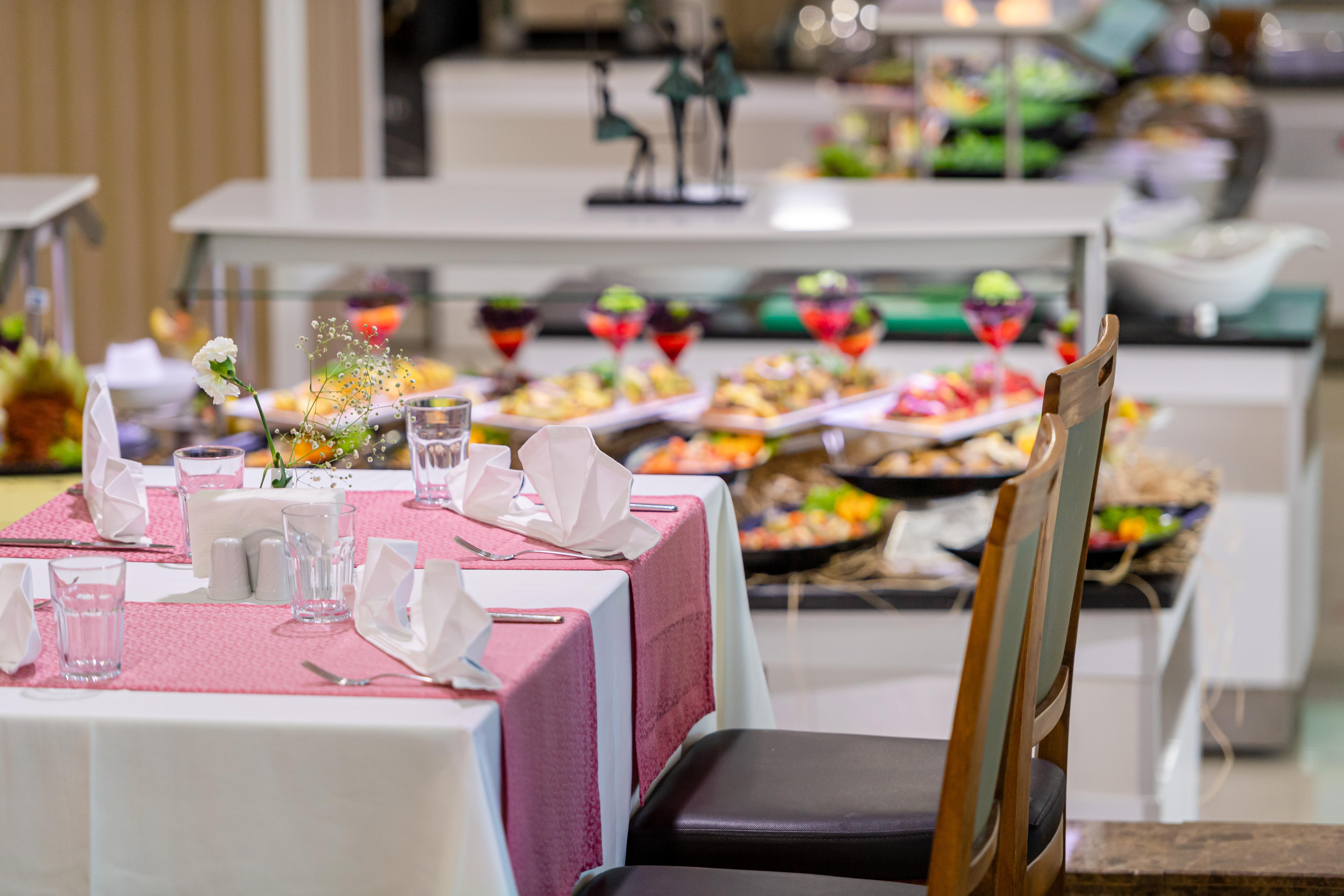 אנטליה Sealife Family Resort Hotel מראה חיצוני תמונה The photo features a dining area of a buffet restaurant. In the foreground, there's a neatly set table with a pink tablecloth, white napkins, and glasses. In the background, a variety of dishes is displayed on a buffet table, showcasing an assortment
