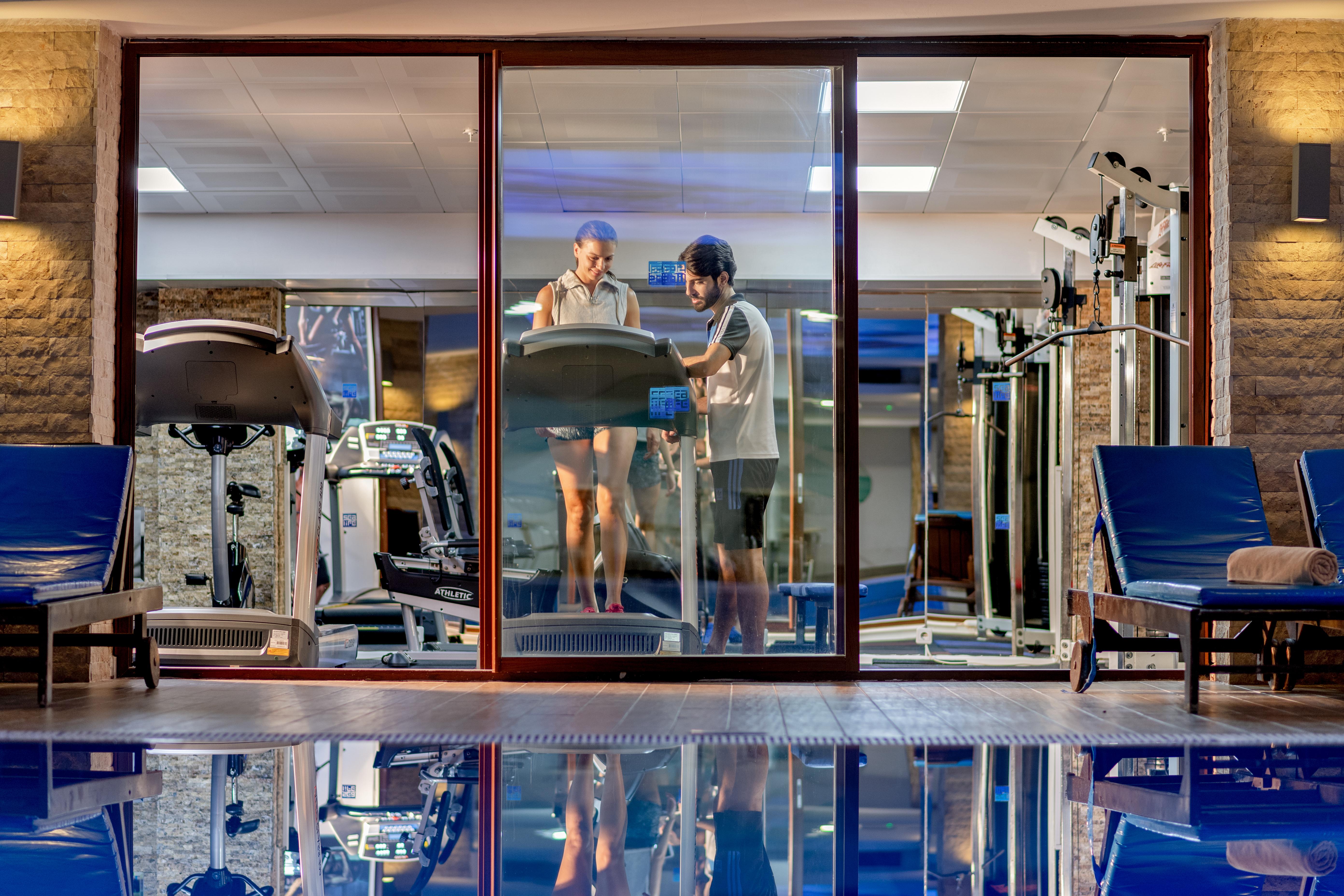 אנטליה Sealife Family Resort Hotel מראה חיצוני תמונה The photo shows a modern gym area viewed through a large glass window. Inside the gym, there are two individuals, one on a treadmill and the other standing beside it, possibly offering guidance or support. The gym is well-equipped, featuring various 