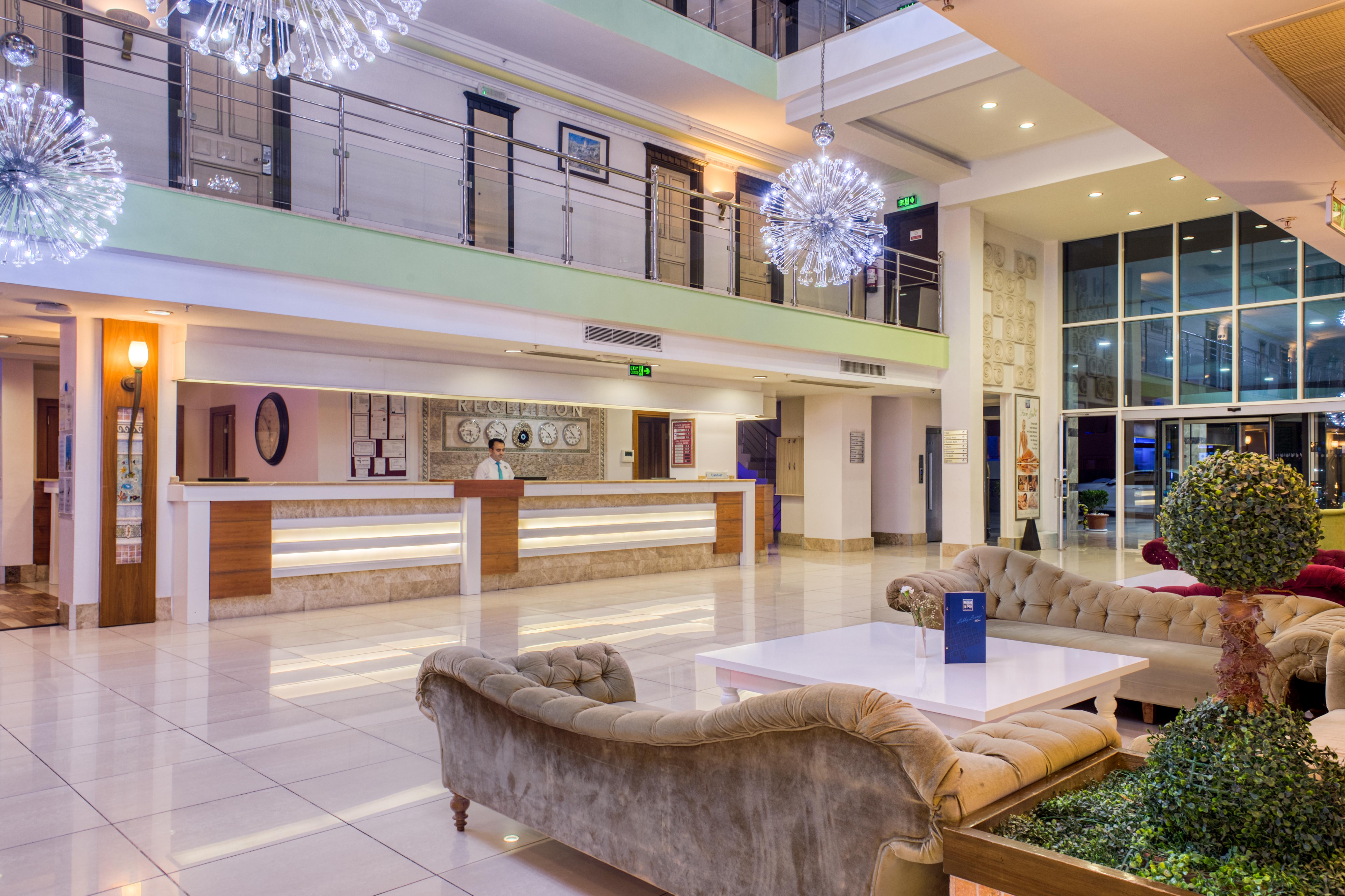 אנטליה Sealife Family Resort Hotel מראה חיצוני תמונה The photo depicts a modern hotel lobby. The space features a spacious and stylish design with large windows allowing natural light to enter. There is a reception desk in the background, along with some decorative elements on the walls. The seating ar