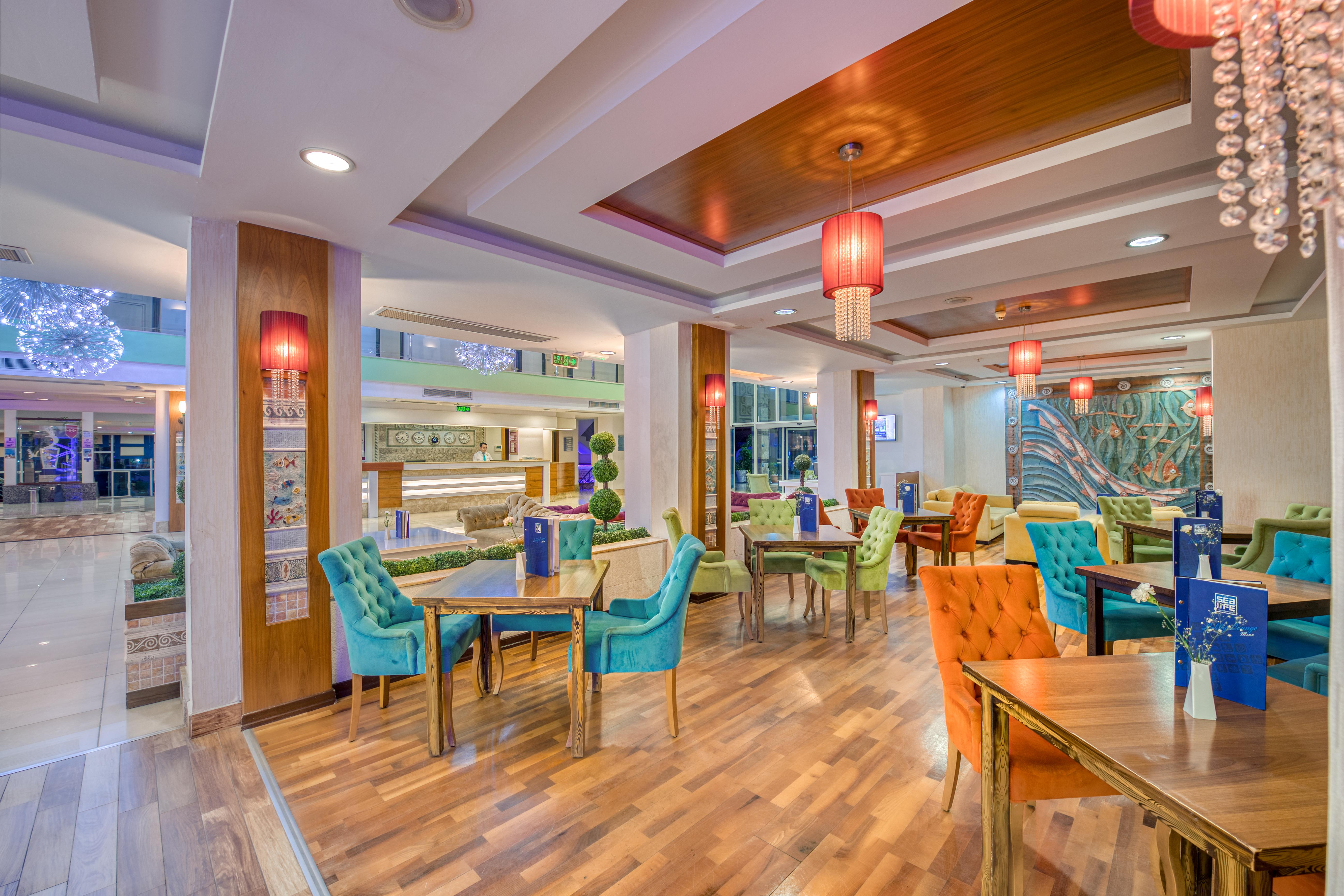 אנטליה Sealife Family Resort Hotel מראה חיצוני תמונה The photo depicts a vibrant and modern restaurant interior. The space features multiple dining tables, each adorned with blue menus. The chairs are brightly colored, in shades of teal, orange, and other hues, adding a playful touch to the decor. The 