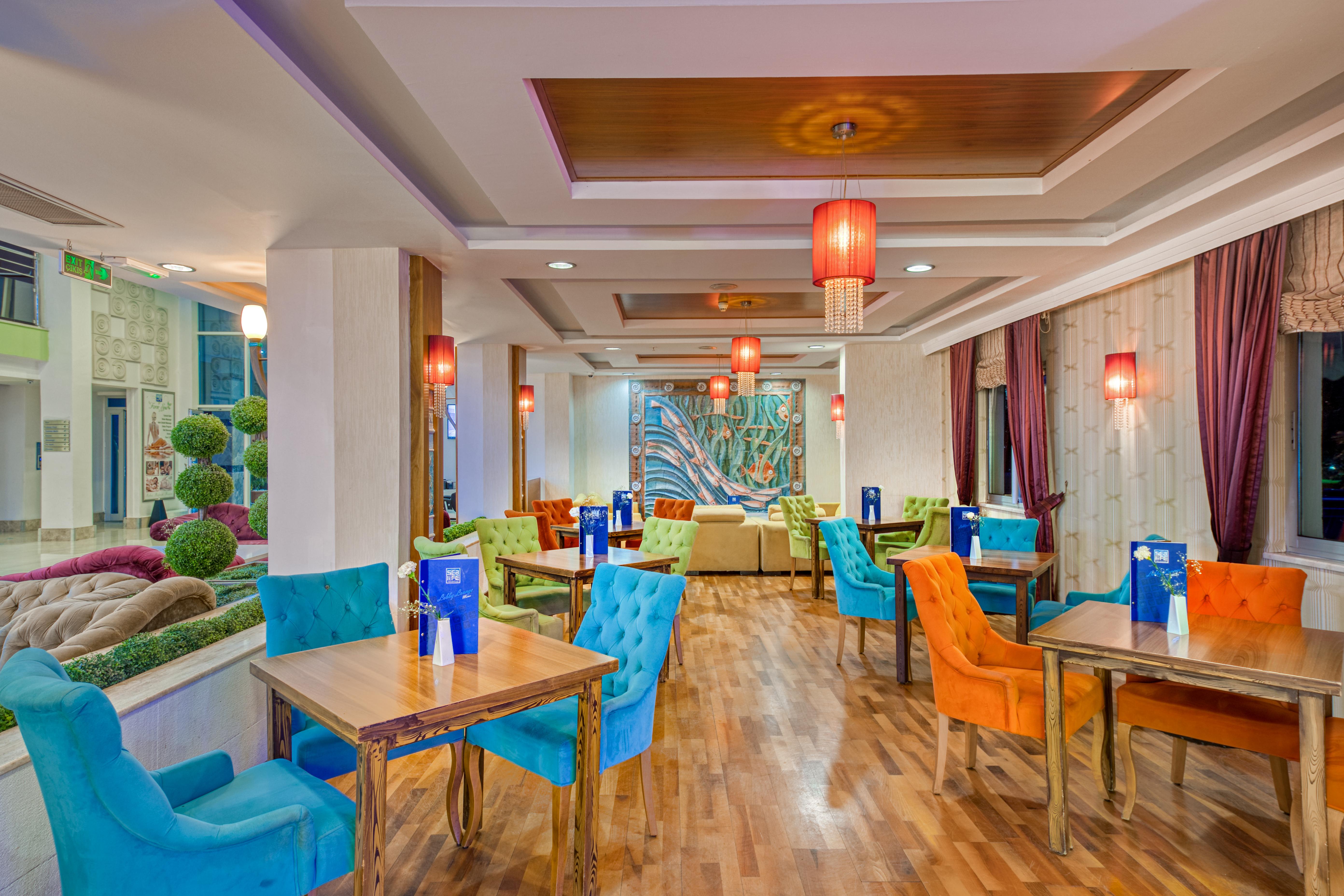 אנטליה Sealife Family Resort Hotel מראה חיצוני תמונה The photo shows a stylish dining area with a contemporary design. The space features a combination of colorful chairs in blue and orange, and wooden tables arranged throughout. The walls have a warm, neutral tone and are complemented by decorative el
