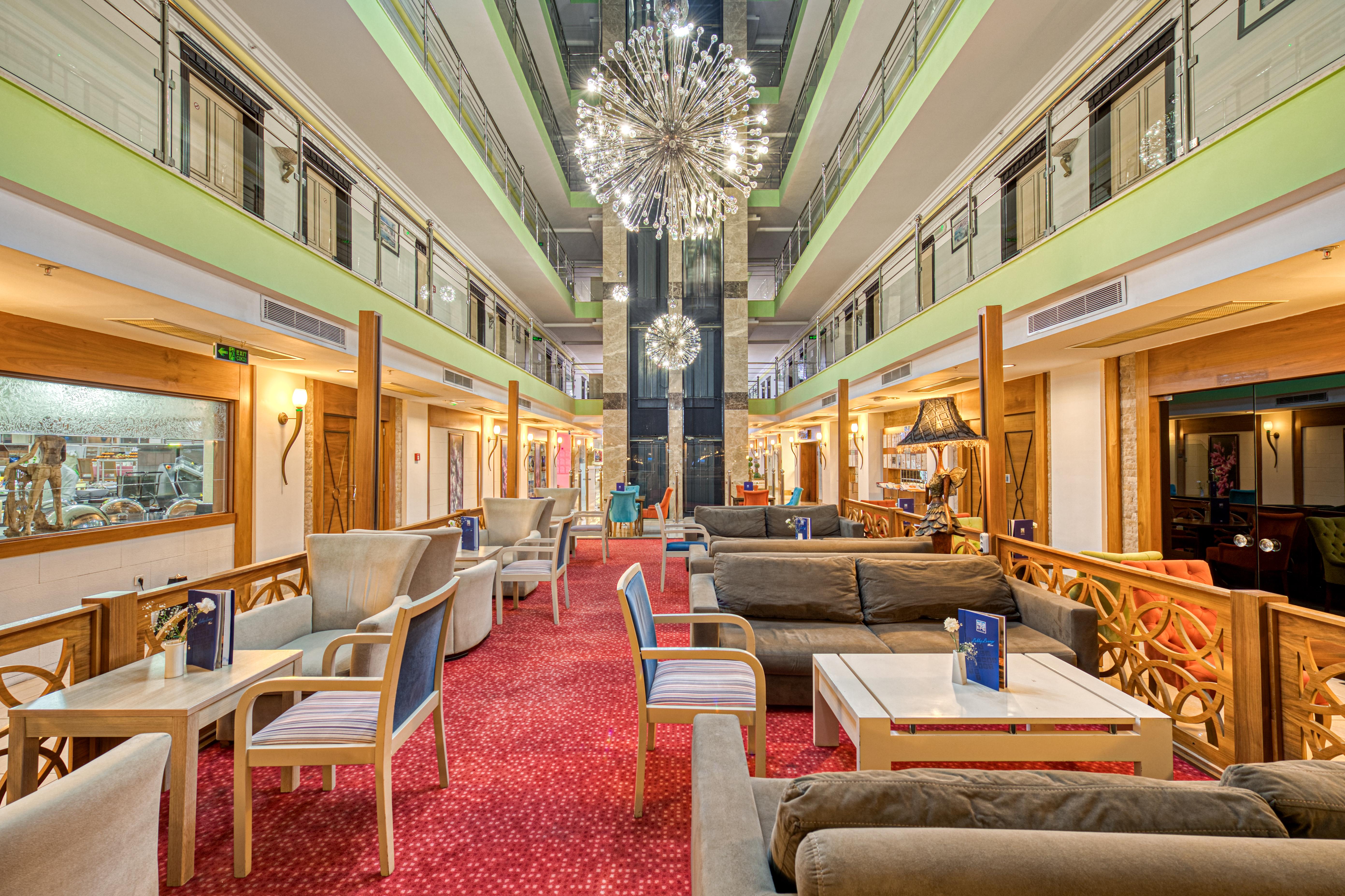 אנטליה Sealife Family Resort Hotel מראה חיצוני תמונה The photo shows a spacious and contemporary hotel lobby with a stylish design. There are comfortable seating areas with plush sofas and chairs arranged around small tables. The floor is covered with a rich red carpet, adding warmth to the space. 

Th