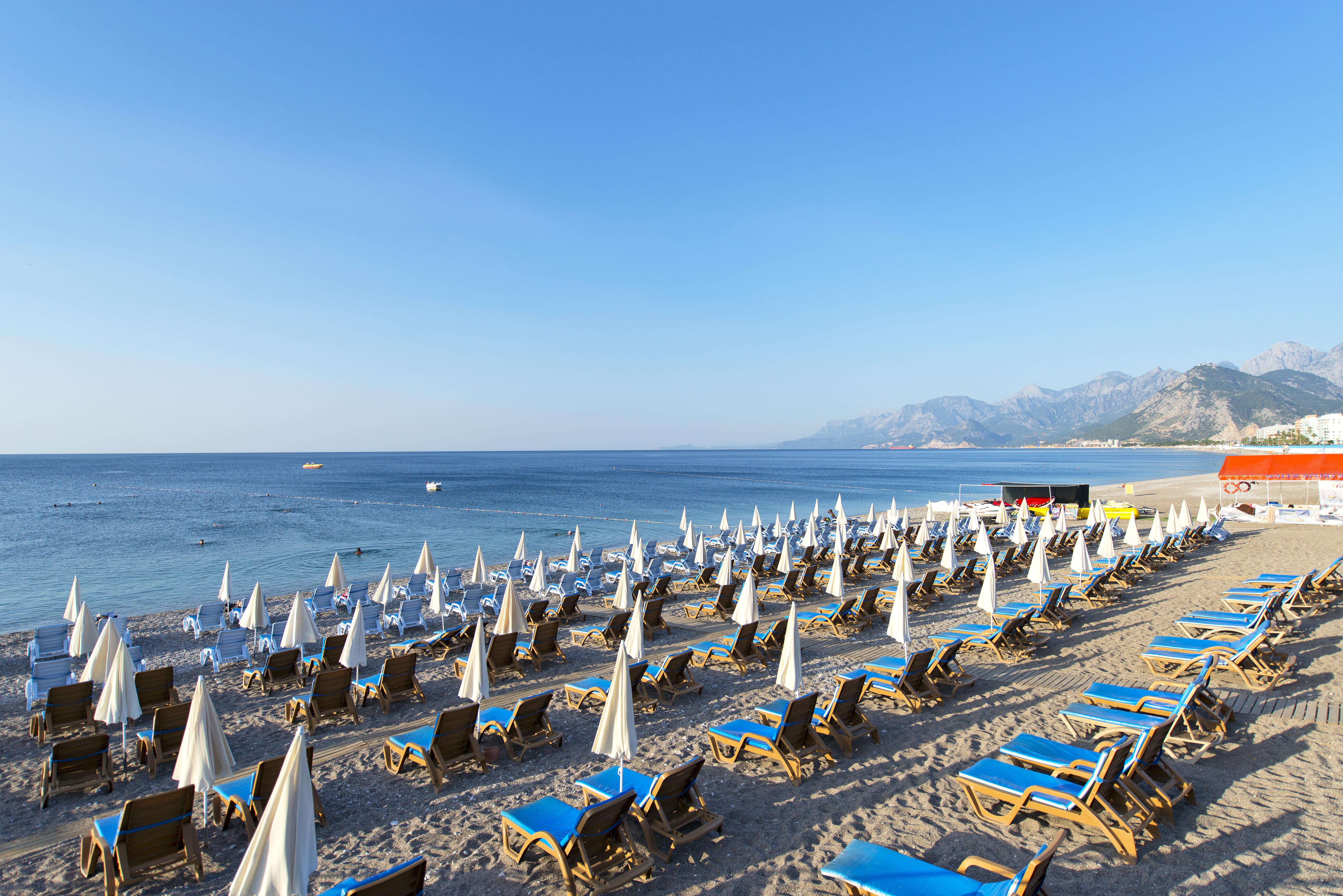 אנטליה Sealife Family Resort Hotel מראה חיצוני תמונה The photo depicts a beach scene with numerous sun loungers arranged in rows on the sand, each equipped with white umbrellas. The loungers are primarily blue, creating a vibrant contrast against the sandy beach. In the background, gentle waves can be 