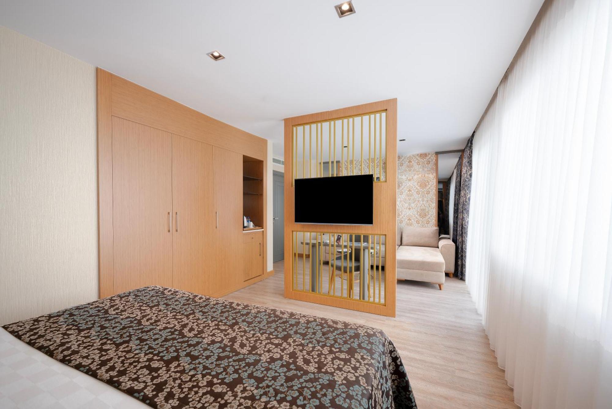 אנטליה Sealife Family Resort Hotel חדר תמונה The photo depicts a modern hotel room designed with a clean and minimalistic aesthetic. It features a spacious layout with wooden flooring and a combination of light and dark colors. 

On one side, there is a bed with a patterned dark bedspread. The 