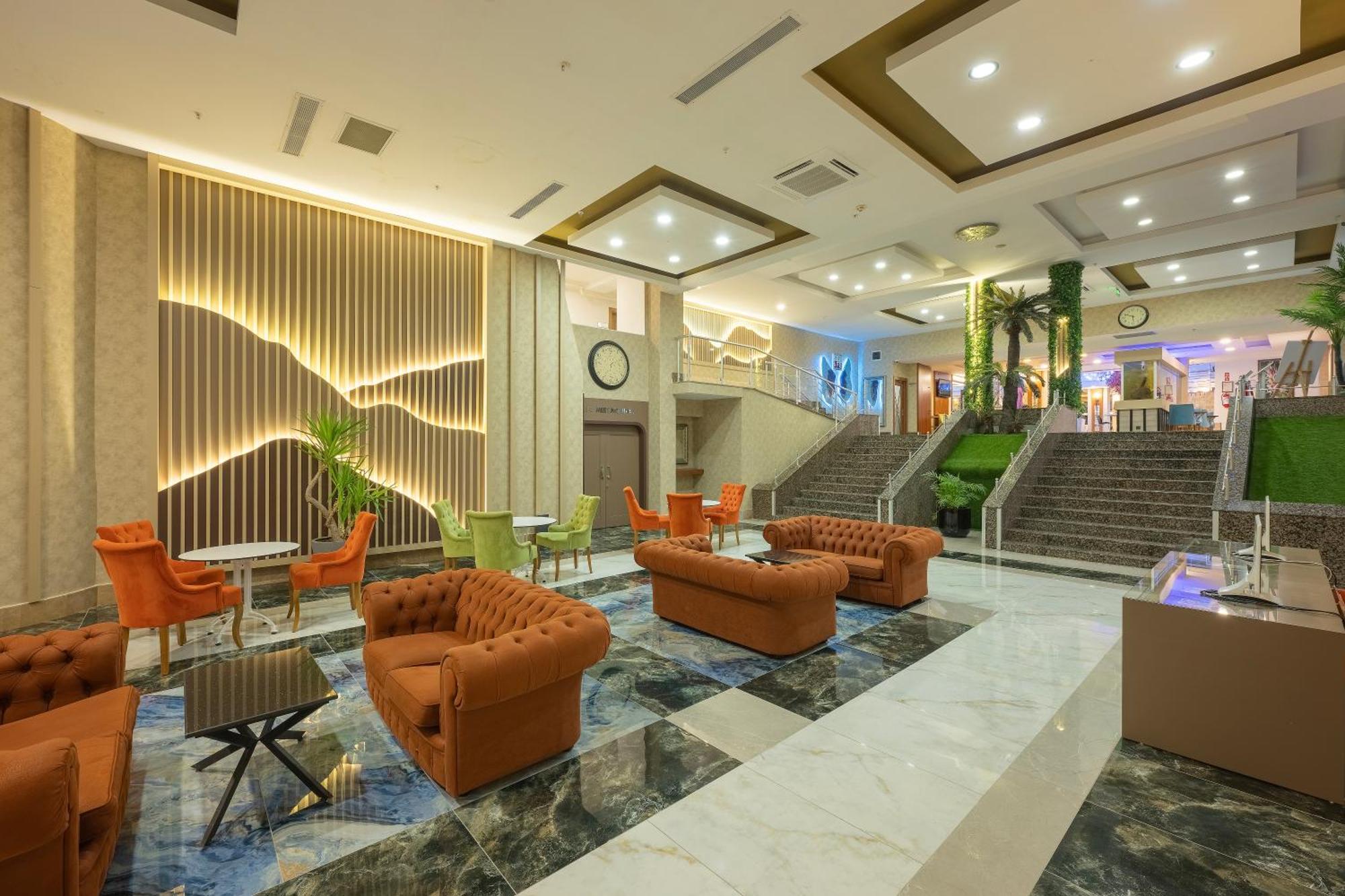 אנטליה Sealife Family Resort Hotel מראה חיצוני תמונה The photo depicts a spacious, modern lobby area within a hotel or similar establishment. The floor features a striking design with dark and light marble patterns. There are several comfortable seating arrangements, including orange upholstered sofas 